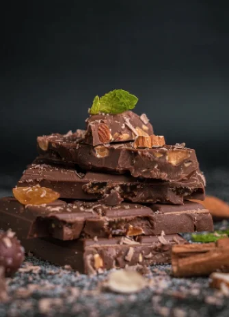 Stack of milk chocolate pieces with almonds, raisins, and a mint leaf on top.